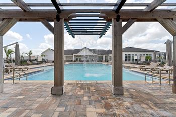 A pool area with a wooden pergola and tiled flooring.